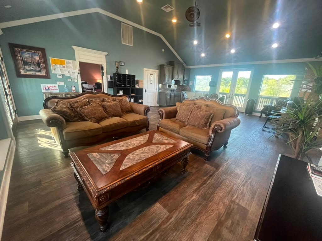 Clubhouse lounge with ornate carved sofas, wood coffee table, vaulted teal ceiling, and kitchenette in background