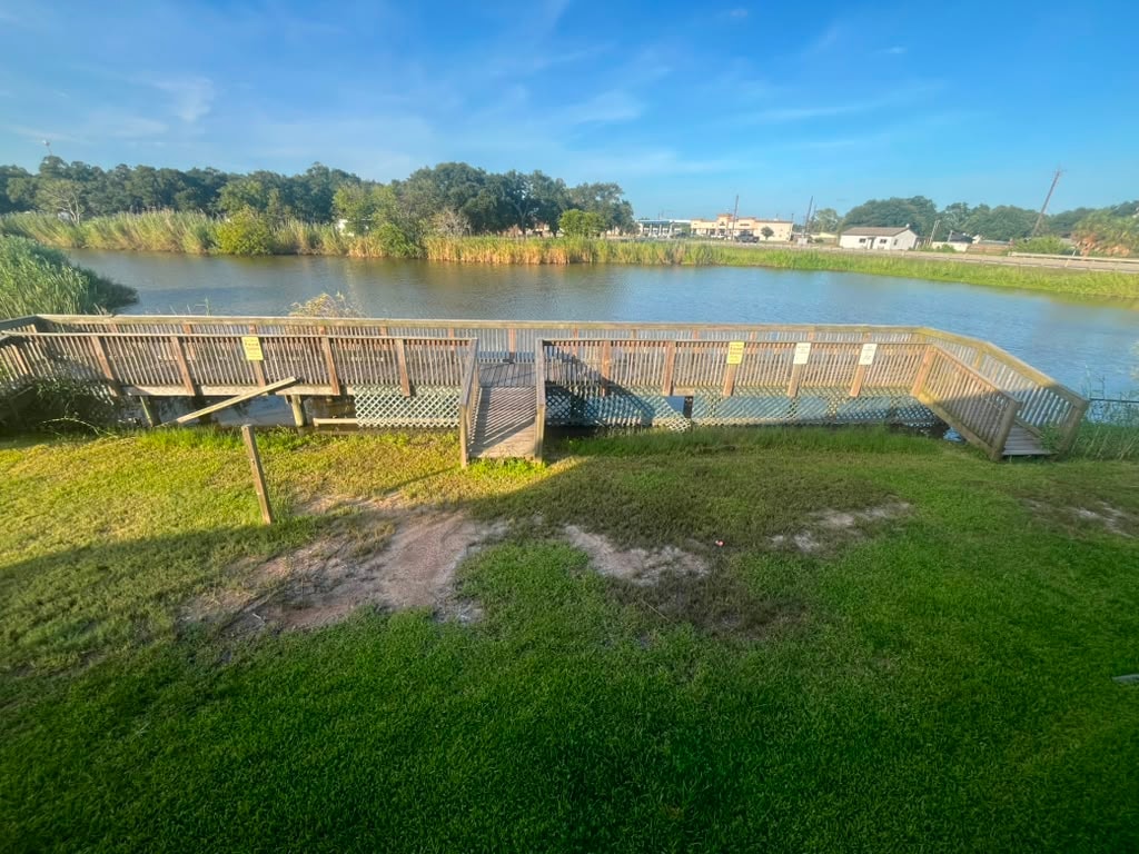 Wooden boardwalk fishing pier over the creek with open water and natural scenery