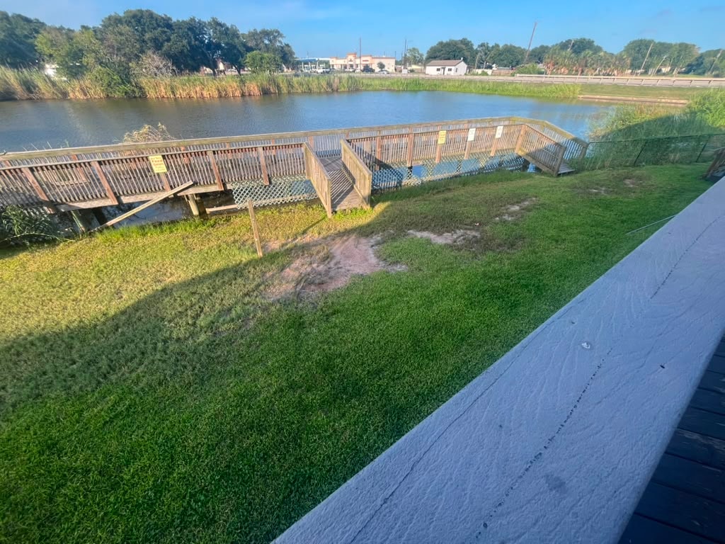Wooden fishing dock extending over the creek with green lawn and waterway views