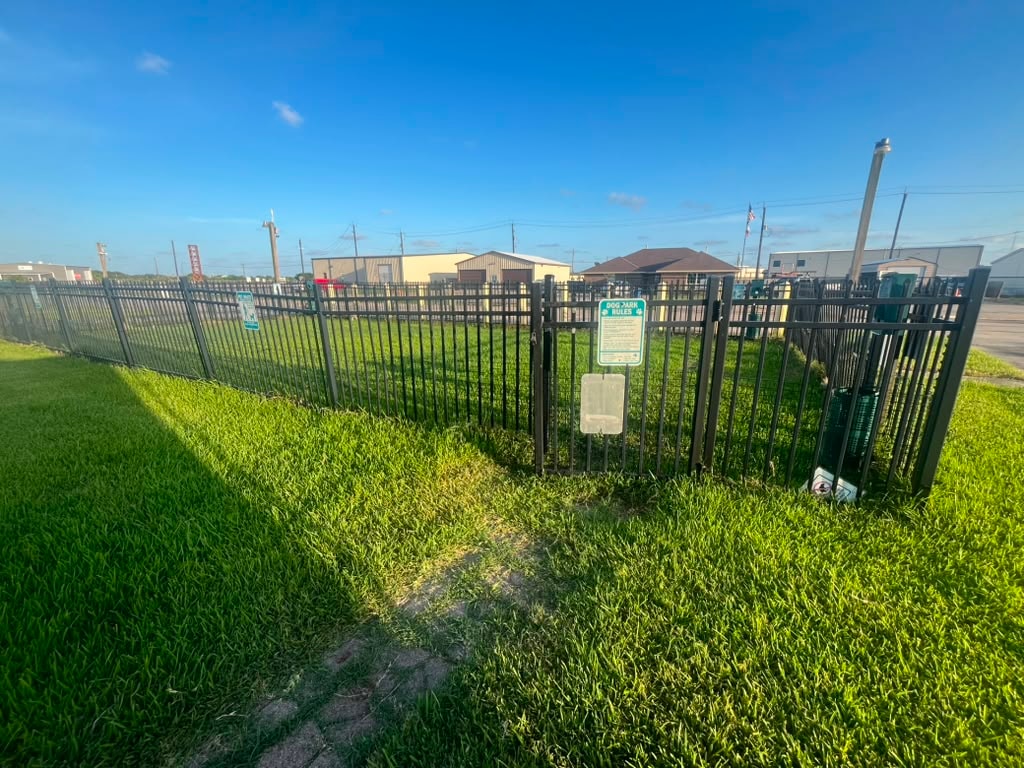 Fenced dog park with iron gate, dog park rules sign, and green grass