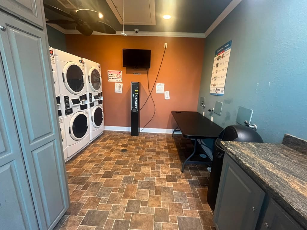 Laundry room interior with stacked washers and dryers, change machine, folding table, and ceiling fan