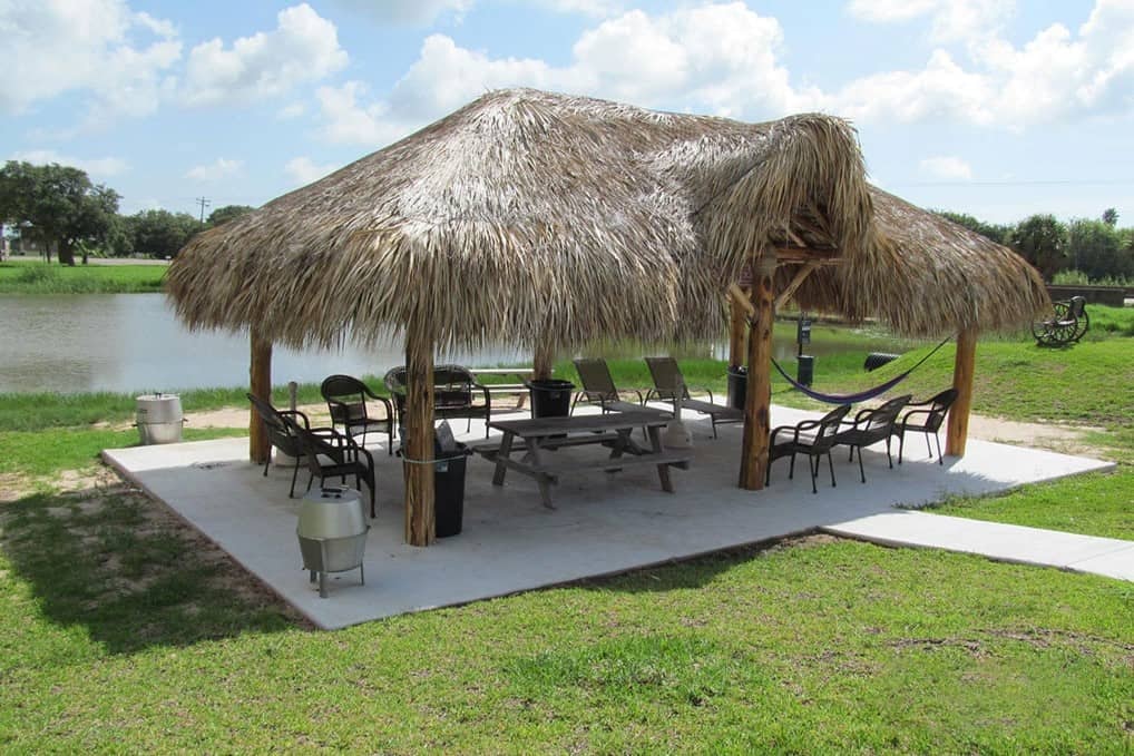 Thatched palapa pavilion with picnic tables, lounge chairs, and hammock overlooking the pond
