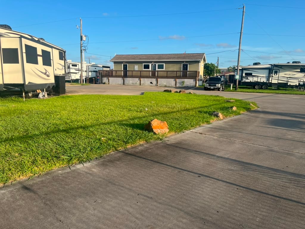 RV sites with fifth-wheels parked on concrete pads, green lawn, and main building in background
